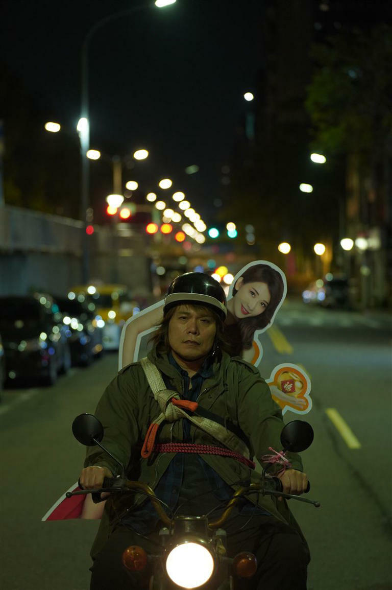 伍佰在《愛情城事》飾演郵差,背著林志玲的看板趴趴走。(圖/華映娛樂提供) 伍佰在《愛情城事》飾演郵差,背著林志玲的看板趴趴走。(圖/華映娛樂提供)